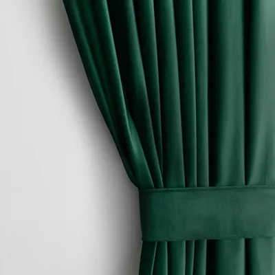 A close-up view of a dark green velvet curtain with pleats and a fabric band.