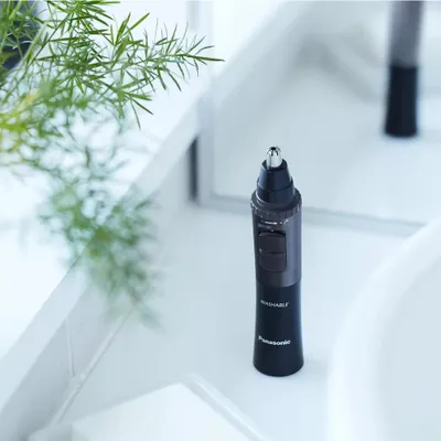A nose hair trimmer sits on a white countertop next to a plant.