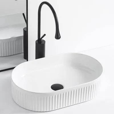 A white oval countertop sink with a black faucet and a reflection in a mirror.
