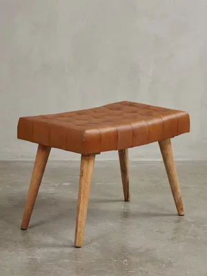 Freigestellter Sitzhocker mit braunem Echtleder-Bezug und Chesterfield-Steppung auf massivem Mangoholz-Gestell, Frontalansicht auf weißem Hintergrund._#sku_BARWL6.012#