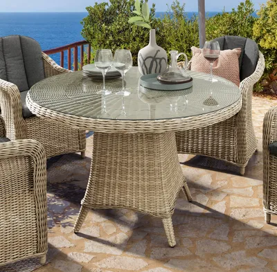 An outdoor dining set with a round table and chairs, set on a patio with a view of the ocean.