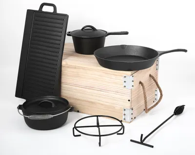 A collection of cast iron cookware items arranged around a wooden crate.
