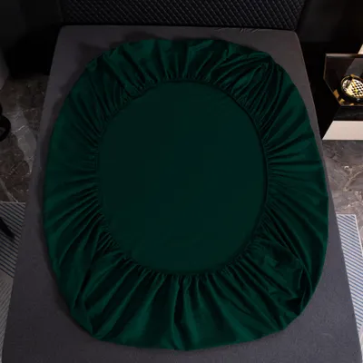 A dark green fitted sheet is laid out on a bed.
