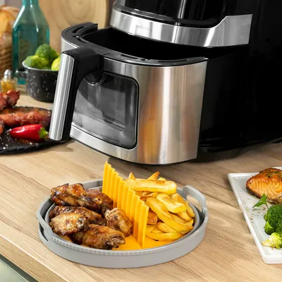 An air fryer with a silicone basket containing chicken wings and french fries.