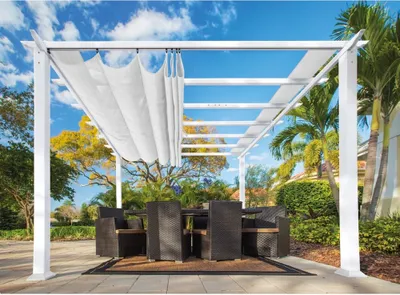 An outdoor dining set under a white pergola with a retractable canopy, set in a garden with palm trees and blue sky.