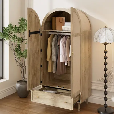 A wardrobe with open doors, showing clothes hanging inside and a drawer pulled out. A plant is to the left, and a floor lamp is to the right.