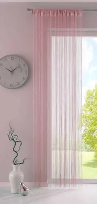 A room interior with a window covered by a pink string curtain, a clock on the wall, and a vase with branches on a table.