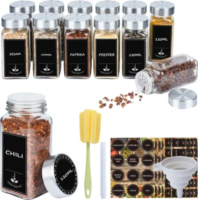 A collection of glass spice jars with silver lids, some filled with spices and others empty, along with accessories like a funnel and a cleaning brush.