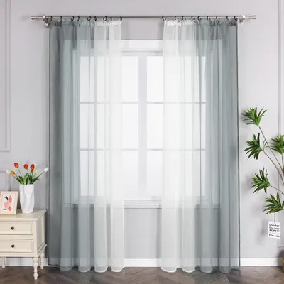 A window with sheer curtains and a small table with a vase of flowers and a framed picture.