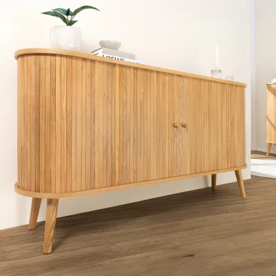 A wooden sideboard with two doors and wooden legs, placed on a wooden floor in front of a white wall.