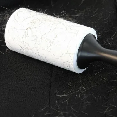 A lint roller covered in pet hair is shown on a black surface, likely a piece of furniture.