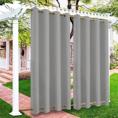 Outdoor curtains hanging on a pergola, with a house and garden in the background.