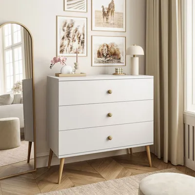 A white dresser with three drawers is placed in a room with a large arched mirror, framed artwork on the wall, and curtains.