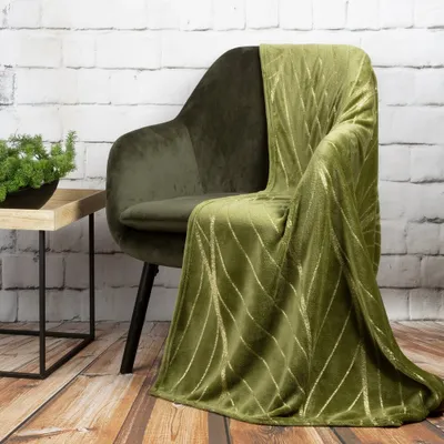A green throw blanket with gold stripes draped over a green armchair, next to a small wooden side table with a plant.