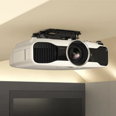 A white projector is mounted to a ceiling with a mounting bracket.