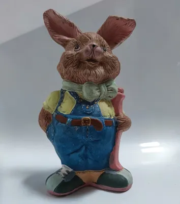Ein Hase, der eine Overall und Schuhe trägt und einen Stock hält. Der Hase hat braunes Fell.