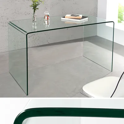 A clear glass desk is shown in a modern setting with a concrete wall and floor.