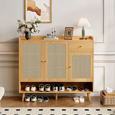 A wooden shoe cabinet with rattan doors and a shelf for shoes, decorated with a vase of flowers, a lamp, and a framed picture.