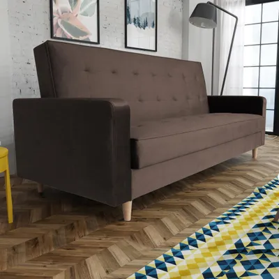 A brown sofa is shown in a room with a brick wall and artwork.