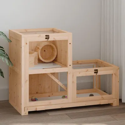 A wooden hamster cage with multiple levels and a running wheel, placed on a wooden floor against a light gray wall.