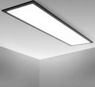 A rectangular LED panel light is mounted on a white ceiling, casting a bright, neutral white light. The image shows the light from a low angle, highlighting its slim profile and the way it illuminates the surrounding ceiling and walls.