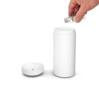 A hand is pouring liquid from a small bottle into a white aroma diffuser.