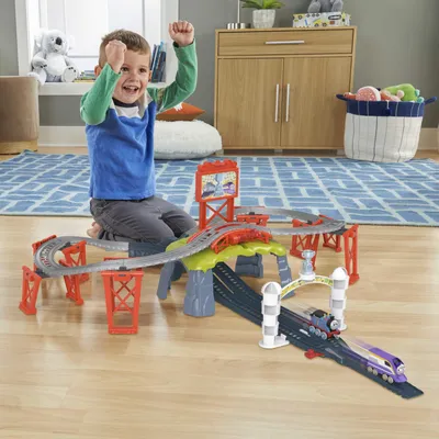 A young boy playing with a toy train set on a wooden floor.