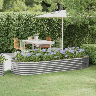 A raised garden bed filled with hydrangeas sits in a garden setting, with a table and chairs under an umbrella in the background.