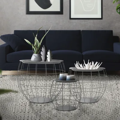 A living room scene featuring a navy blue sofa and a set of three round metal side tables with wire basket bases.