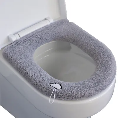 A close-up view of a gray, plush toilet seat cover on a white toilet.