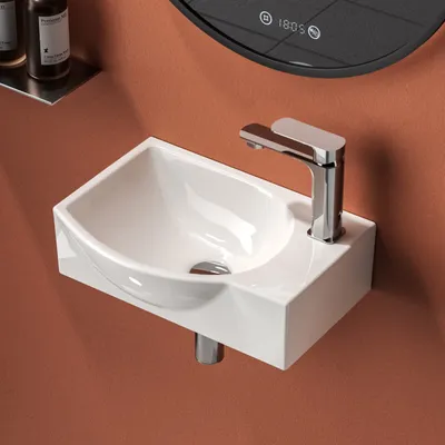 A close-up shot of a white ceramic washbasin with a chrome faucet mounted on an orange wall.