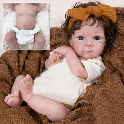 Immagine prodotto di 45 cm di altezza, corpo in plastica/cotone, occhi azzurri, trapianto di capelli, ciglia adesive. Tutina a maniche corte color beige, fascia per capelli marrone con fiocco, calzini bianchi. Bambola realistica.
