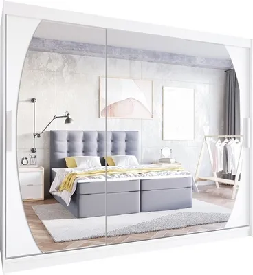 A bedroom scene reflected in mirrored wardrobe doors, showing a bed, nightstand, and clothing rack.