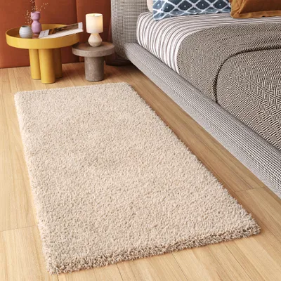 A beige rug is placed on a wooden floor next to a bed and a side table.