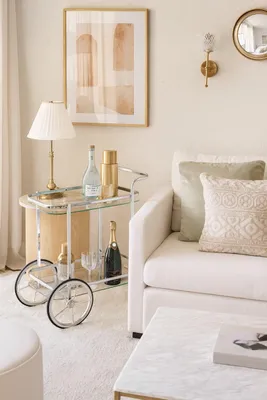 A stylish bar cart filled with drinks and glassware, placed next to a sofa in a well-decorated living room.
