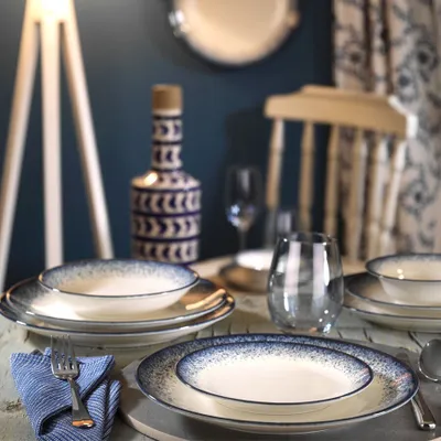 A table setting with dinnerware, a decorative vase, and a chair in the background.