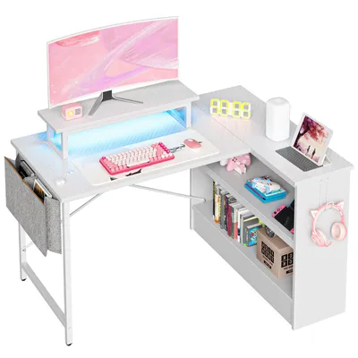 A white L-shaped desk with a monitor, keyboard, mouse, laptop, and shelves filled with books and accessories.