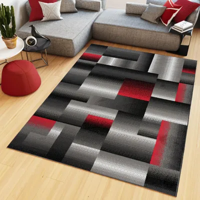 A modern living room with a sectional sofa, a rug, and a small red ottoman.