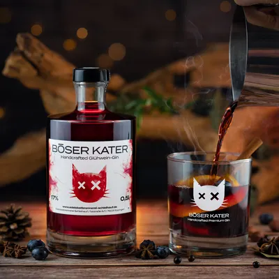 A bottle of red gin and a glass of hot drink with garnishes, set against a rustic, festive background.