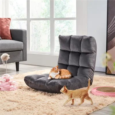 Two cats are playing on a fluffy rug in front of a window. One cat is sleeping on a floor chair, and another is walking on the rug. There are cat toys on the rug.