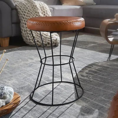 A brown leather stool with a black wire frame sits on a gray rug.