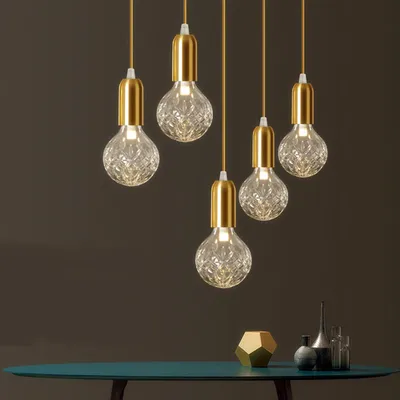 A group of six pendant lights with gold fixtures and clear, textured glass bulbs hang against a dark gray background.
