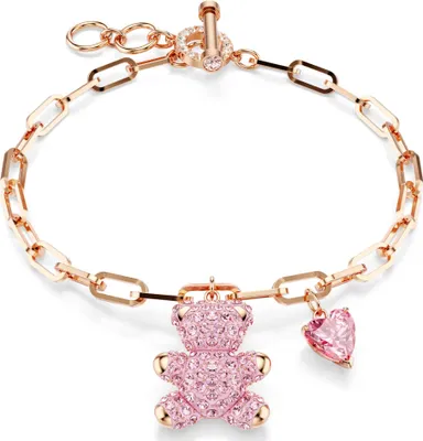 A rose gold chain bracelet with a pink teddy bear charm and a pink heart charm, set against a white background.