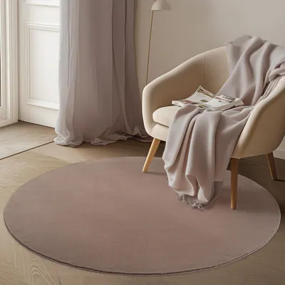 A round rug is placed on a wooden floor in front of a chair with a blanket and a magazine.