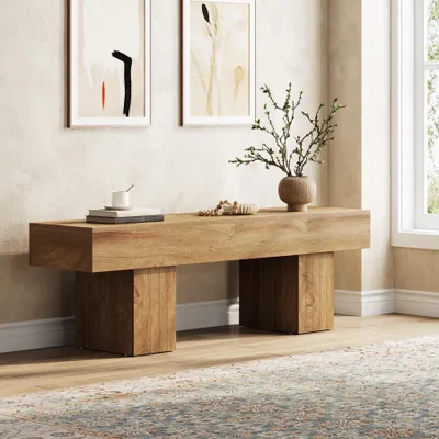 A wooden bench in a room with artwork on the wall and a rug on the floor.