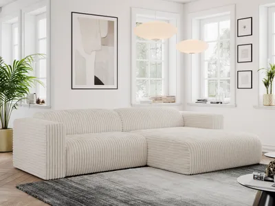 A modern living room with a large, beige corduroy sectional sofa as the focal point. The sofa is placed on a rug in front of a window with natural light streaming in. Artwork and plants add decorative elements to the scene.