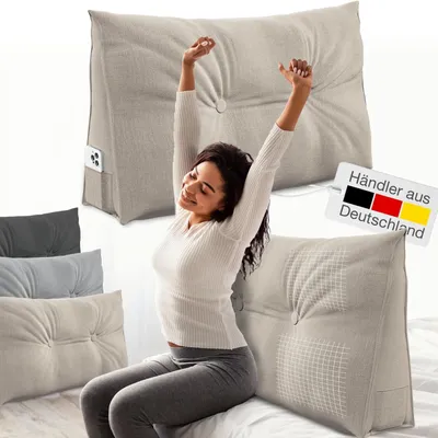 A woman is stretching while sitting on a bed with several pillows around her.