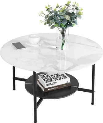 A round coffee table with a marble-like top and a black shelf underneath, decorated with a vase of flowers, a phone, and a cup.