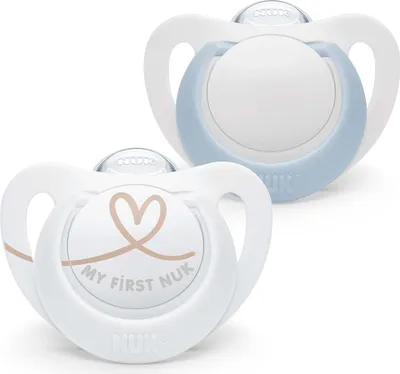 Two NUK pacifiers are shown against a white background. One pacifier is in the foreground and has a heart and text "MY FIRST NUK" printed on it. The other pacifier is in the background and has a light blue rim.