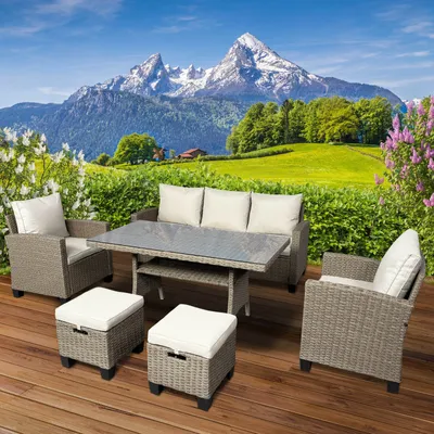 A polyrattan garden seating set is arranged on a wooden deck with a scenic mountain and meadow backdrop.